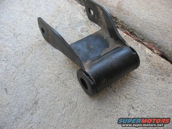 Black metal leaf spring shackle with rubber bushings, resting on concrete