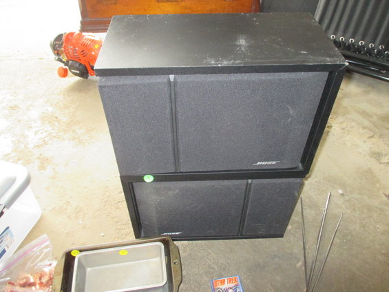 Two black Bose speakers stacked, with a weed trimmer and baking pan nearby
