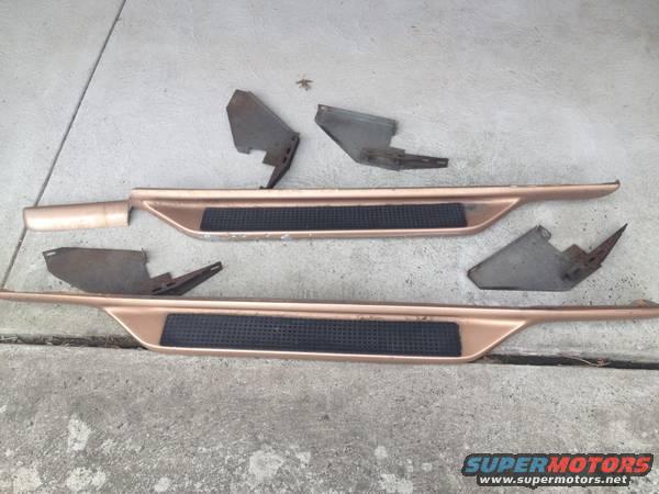 pair of bronze running boards with black grip tape and several metal brackets