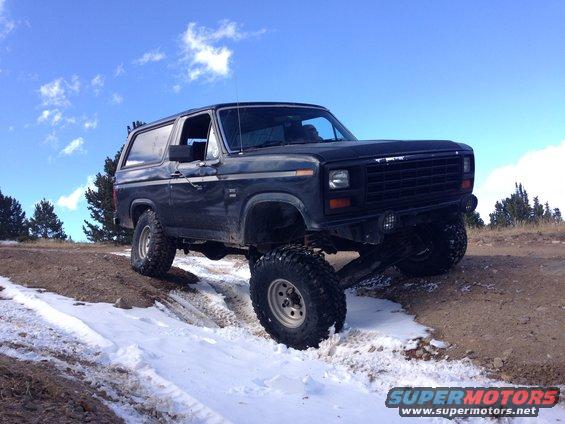 Black Ford Bronco with lifted suspension driving on a snowy dirt road