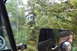 1983 Ford Bronco - The vehicle is driving on a dirt road surrounded by trees and foliage.