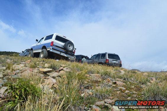 White and blue Ford Bronco with spare tire on rear, parked on rocky terrain