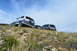 1983 Ford Bronco - Several SUVs navigate a rocky, grassy hillside under a cloudy sky.