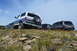 1983 Ford Bronco - A white and blue 1992 Ford Bronco is seen from the rear, parked on a rocky hill alongside other vehicles.