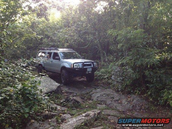 Silver Nissan Frontier driving on a rocky trail through trees