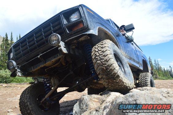 Black SUV with large tires climbing over rocks. Driver visible in cab