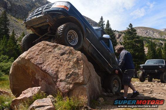 Dark blue SUV climbing a rock, with another SUV behind it