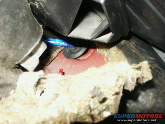 Close-up of frayed insulation and wiring under a car's dashboard, with a blue light visible