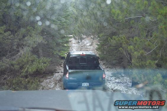 Pickup truck driving on a muddy, tree-lined dirt road