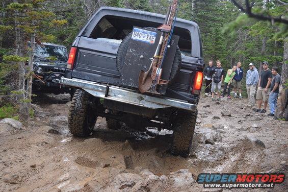 Black Ford Bronco navigating a muddy, rocky trail with a group of people watching