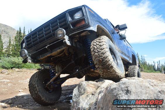 Blue off-road SUV with large tires climbing over rocks on a dirt trail