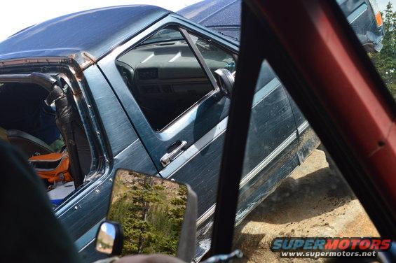 Side view of a teal Ford F-Series truck with a damaged roof, parked on dirt. Interior visible
