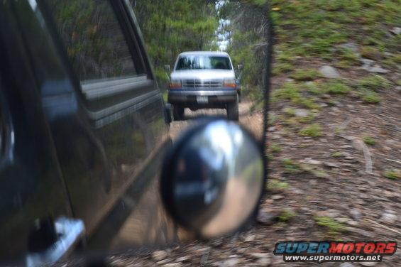 Silver Ford F-Series truck on a dirt road, seen from another vehicle's side mirror