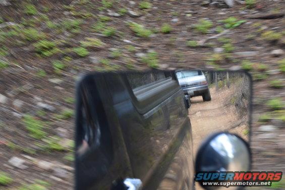 Silver SUV reflected in side mirror on dirt road