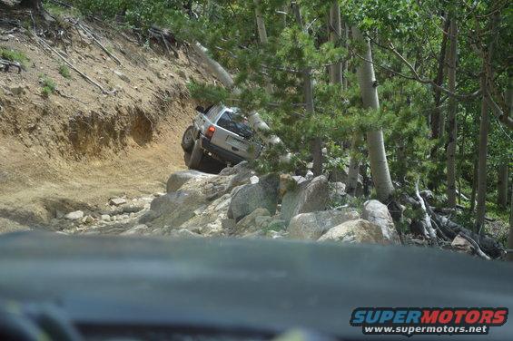 Silver SUV navigating a steep, rocky trail with trees on the right