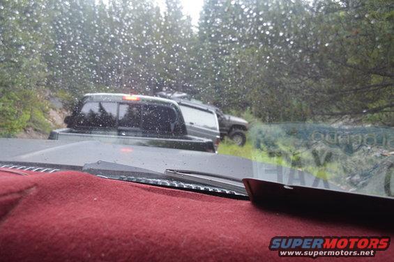 View from inside a vehicle looking at two SUVs on a wet, wooded dirt road