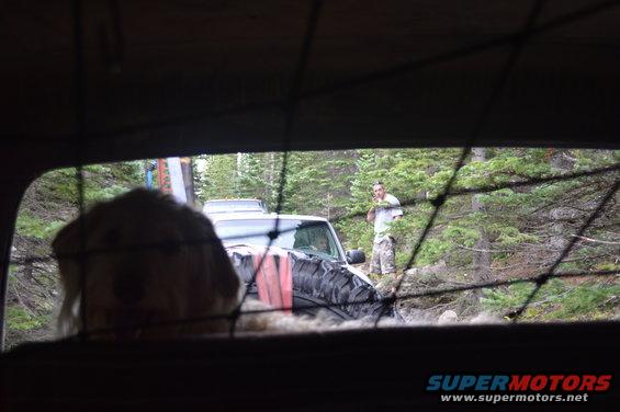 Off-road vehicles in woods, one with large tire, person standing nearby