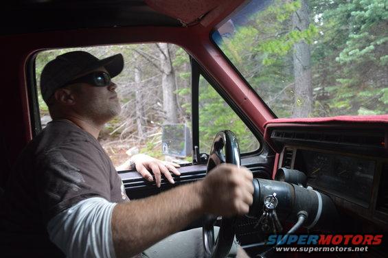 Man wearing a cap and sunglasses drives a truck through a wooded area