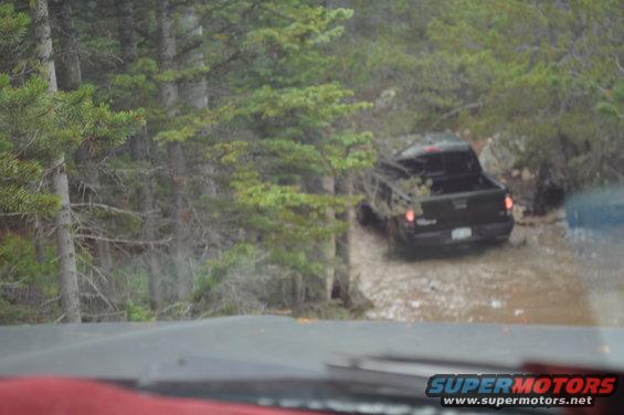 Black pickup truck driving through muddy water in a wooded area