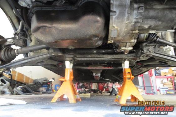 Underbody view of a car on jack stands, showing suspension and drivetrain components