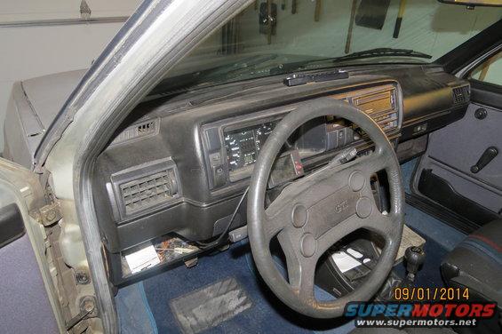 1985 Volkswagen GTI interior showing dashboard, steering wheel with GTI logo, and blue carpet