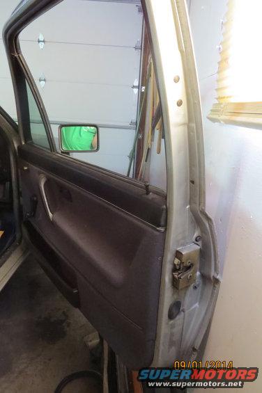 Car door interior with brown panel, silver handle, and side mirror reflecting a green shirt