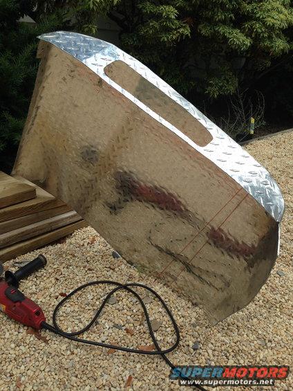 Shiny metal object with diamond plate trim and cutouts, next to a power tool and lumber