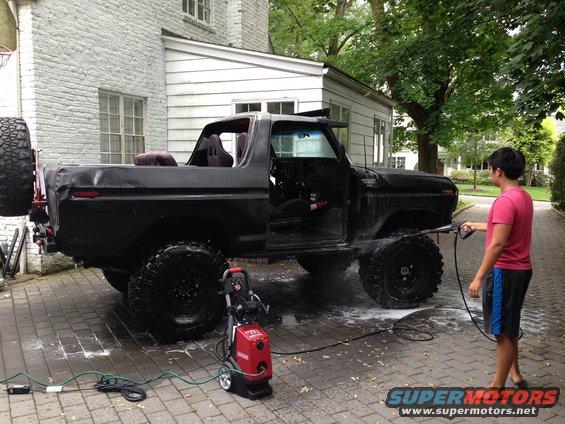 Black 1979 Ford Bronco with aftermarket wheels and tires being pressure washed in a driveway