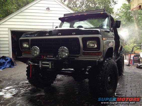 Front view of a lifted black Ford F-Series truck with a light bar on top, parked in front of a garage