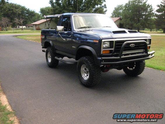 Blue Ford Bronco with aftermarket bumper and light bar parked on asphalt