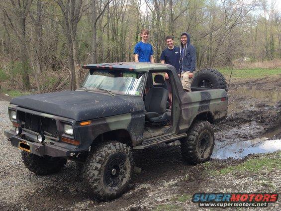 Camouflaged 1978 Ford F-150 pickup truck modified for off-roading, stuck in mud with three people standing on it