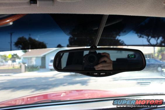 Interior rearview mirror showing reflection of camera and hand, with a digital display showing 'SW'