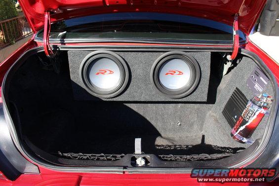 Car trunk interior showing two subwoofers in a box and a car amplifier