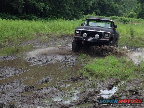Black 1979 Ford Bronco driving through mud, front view with winch and light bar