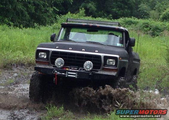 Black 1979 Ford F-150 truck driving through mud with a light bar on the roof