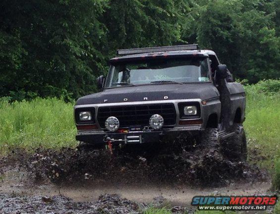 Ford F-Series truck driving through mud, has a light bar on top and winch on front
