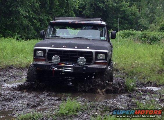 Black 1978 Ford Bronco driving through mud, front view