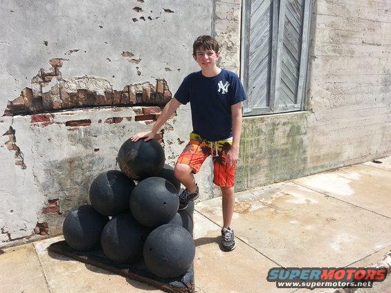Kid posing with a stack of cannonballs in front of a weathered wall