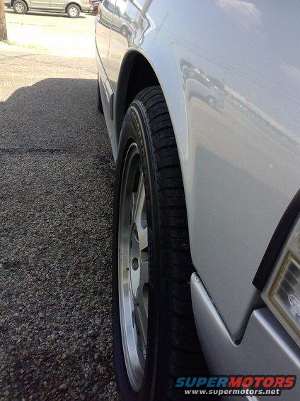 Silver car wheel and fender, side view. Watermark 'SUPERMOTORS.NET'