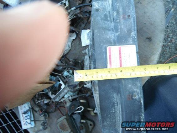 Radiator support measured with tape measure, showing a red and white label