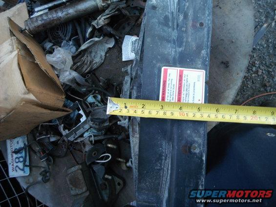 Pile of scrap metal, car parts, and a measuring tape next to a warning label