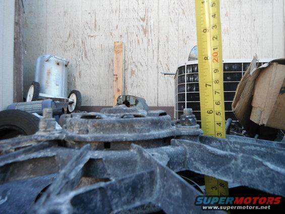 Close-up of a radiator fan with a yellow measuring tape next to it, showing about 8 inches. An air conditioning unit is in the background