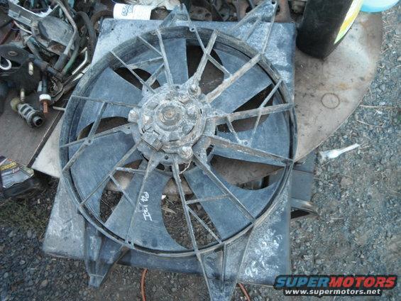 Radiator fan with black plastic blades and a central motor housing, resting on a metal frame