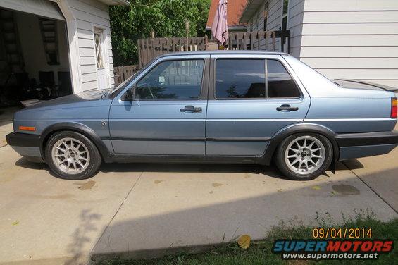 Side view of a blue 1990 Volkswagen Jetta with aftermarket wheels parked on a driveway
