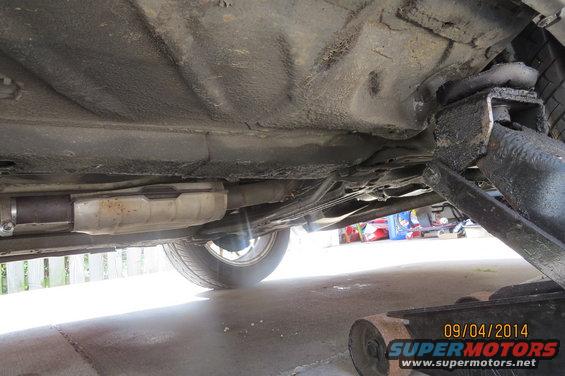 Underside of car showing catalytic converter and exhaust pipe, jack visible