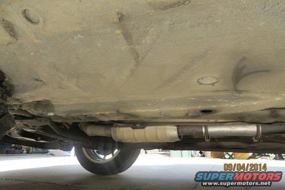 Underside view of a vehicle showing exhaust pipe, catalytic converter, and wheel