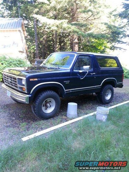 Dark blue Ford Bronco parked outside a building with trees in the background