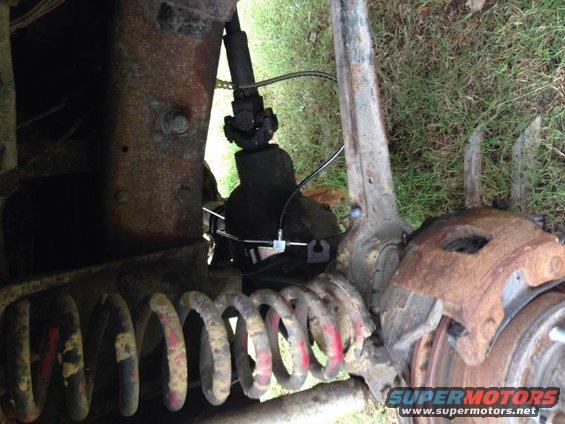 close-up of rusty front suspension, coil spring, brake caliper, and driveshaft U-joint