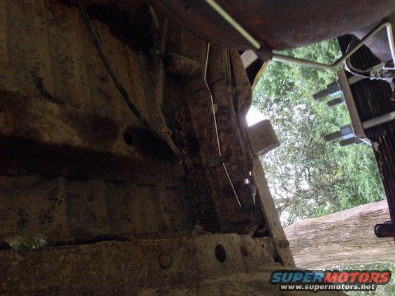 Close-up of heavily rusted metal frame and suspension parts of a vehicle, with trees visible in the background
