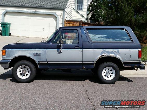 Two-tone blue and silver Ford Bronco with rust spots and peeling paint, seen from the side
